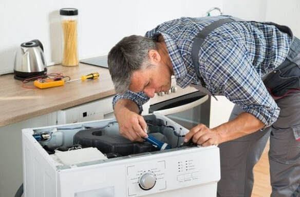 McKinney Appliance repairman fixing a whirlpool washer. The washing machine is pulled out of the counter and he is repairing the appliance with his tool.