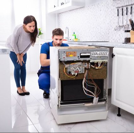 Frisco appliance repair man fixing a built in dishwasher that has been pulled out from its space in the counter. A female customer looks at the repair, while he explains the problem to her