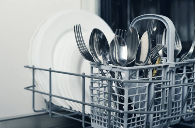 A close up picture of the bottom rack of a dishwasher that is pulled out and clean utensils neatly stacked in the holder.